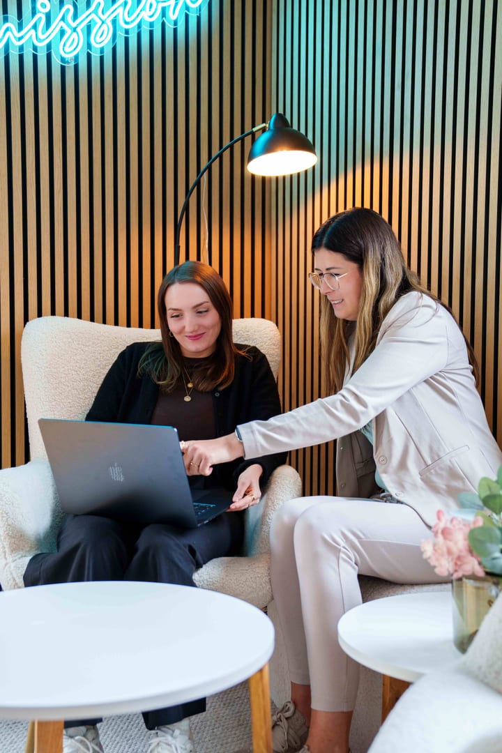 Zwei MediaOne Kolleginnen besprechen ein Projekt am Laptop in der Lounge